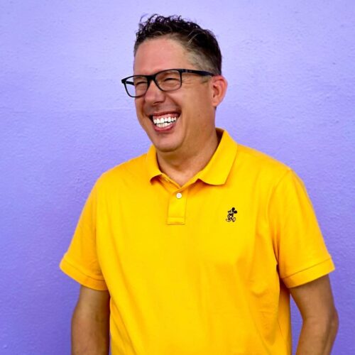 Joyful man in yellow polo shirt smiling on purple background for church community event.