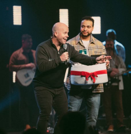 Two pastors on stage holding a wrapped gift basket during a Christmas service
