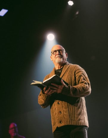 A pastor holding a Bible under a spotlight on stage
