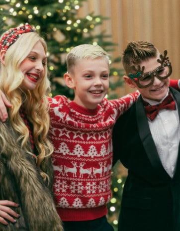 Three kids in festive Christmas outfits smiling together