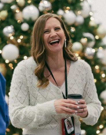 A volunteer laughing with a coffee in front of a decorated Christmas tree
