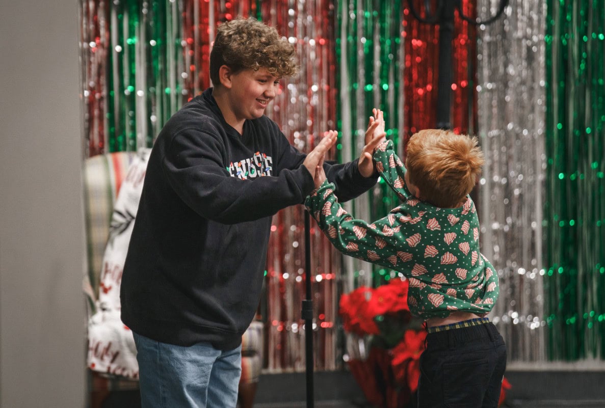 A pastor and a young boy high-five in front of red and green tinsel at a church Christmas event