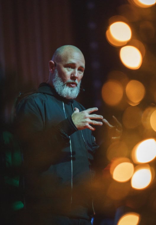 A pastor speaking on stage with warm Christmas lights glowing behind him